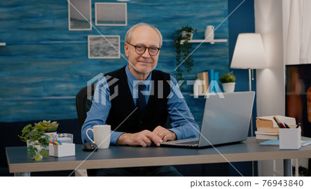 Senior man looking at camera smiling sitting in workplace at desk 76943840