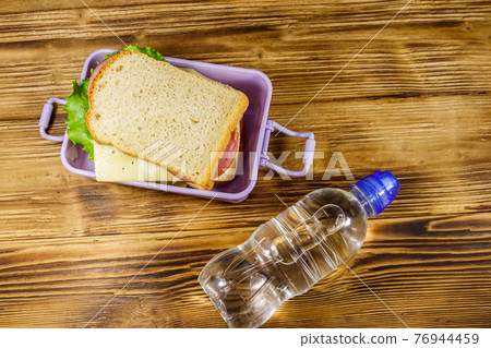 Lunch box with sandwiches and bottle of water on a wooden table. Top view 76944459