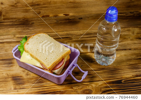 Lunch box with sandwiches and bottle of water on a wooden table Lunch box with sandwiches and bottle of water on a wooden table 76944460