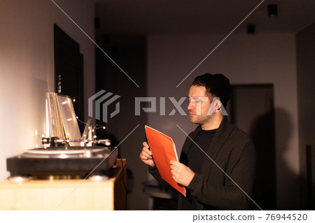 Young unshaven handsome hipster guy puts record on turntable from red envelope 76944520