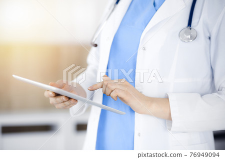 Unknown woman-doctor standing in sunny clinic and using tablet pc, close-up. Data and best service in medicine Unknown woman-doctor standing in sunny clinic and using tablet pc, close-up. Data and best service in medicine 76949094