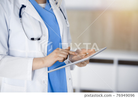 Unknown woman-doctor standing in sunny clinic and using tablet pc, close-up. Data and best service in medicine Unknown woman-doctor standing in sunny clinic and using tablet pc, close-up. Data and best service in medicine 76949096