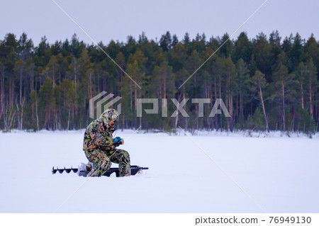 ice fishing. fisherman fishing on a winter lake against a background of forest. ice fishing. fisherman fishing on a winter lake against a background of forest. 76949130