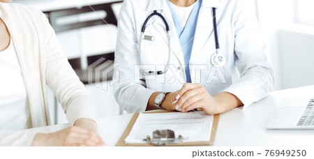 Unknown woman-doctor sitting and communicating with female patient. Physician checks medical history record and exam results, close-up. Healthcare concept 76949250