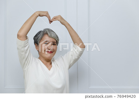 Silver-haired woman showing heart shape 76949420