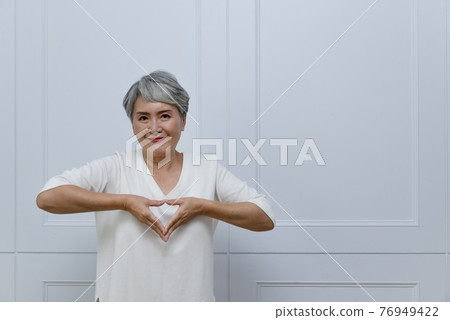 Silver-haired woman showing heart shape Silver-haired woman showing heart shape 76949422