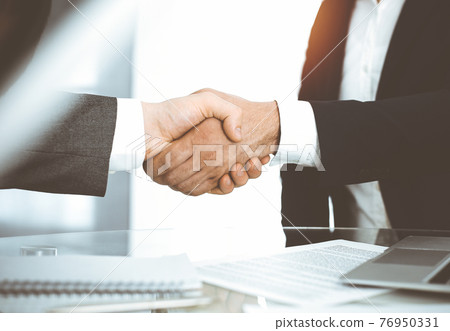Unknown diverse business people are shaking hands finishing contract signing in sunny office, close-up. Business handshake concept Unknown diverse business people are shaking hands finishing contract signing in sunny office, close-up. Business handshake concept 76950331