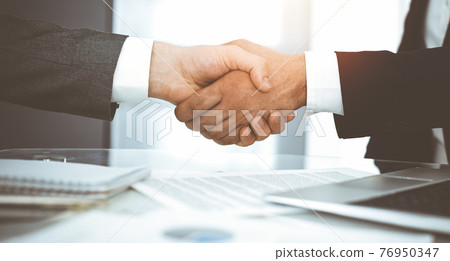 Unknown diverse business people are shaking hands finishing contract signing in sunny office, close-up. Business handshake concept Unknown diverse business people are shaking hands finishing contract signing in sunny office, close-up. Business handshake concept 76950347