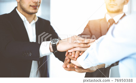 Business people group showing teamwork, joining hands and giving five to each other in sunny office Business people group showing teamwork, joining hands and giving five to each other in sunny office 76950388