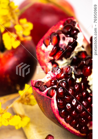 ruby red, juicy pomegranate open on a table with apple and dry yellow flowers 76950969