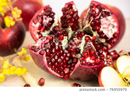 ruby red, juicy pomegranate open on a table with apple and dry yellow flowers 76950970