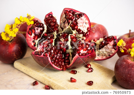 ruby red, juicy pomegranate open on a table with apple and dry yellow flowers 76950973