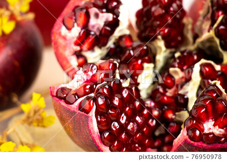 ruby red, juicy pomegranate open on a table with apple and dry yellow flowers 76950978