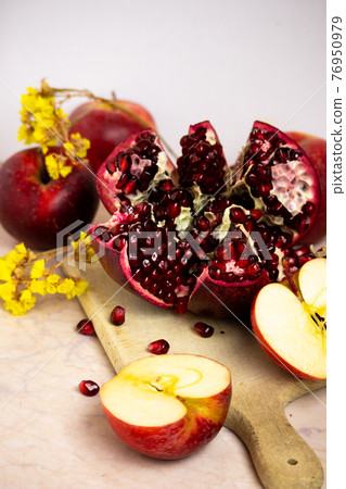 ruby red, juicy pomegranate open on a table with apple and dry yellow flowers 76950979