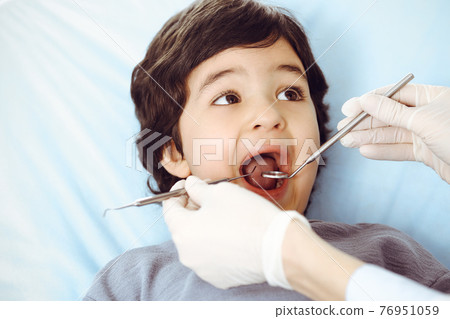 Cute arab boy sitting at dental chair with open mouth during oral checking up with doctor. Visiting dentist office. Stomatology concept Cute arab boy sitting at dental chair with open mouth during oral checking up with doctor. Visiting dentist office. Stomatology concept 76951059