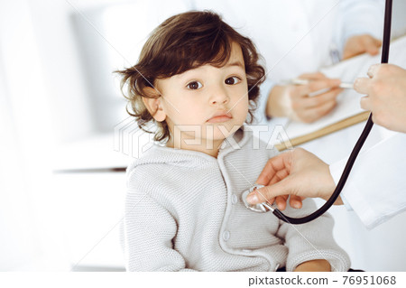Woman-doctor examining a child patient by stethoscope. Cute arab toddler at physician appointment. Medicine concept Woman-doctor examining a child patient by stethoscope. Cute arab toddler at physician appointment. Medicine concept 76951068