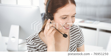 Casual dressed young woman using headset and computer while talking with customers online. Group of operators at work. Call center, business concept Casual dressed young woman using headset and computer while talking with customers online. Group of operators at work. Call center, business concept 76951250