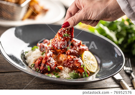 Spicy glazed chicken thighs and wings served with rice and coriander leaves 76952576