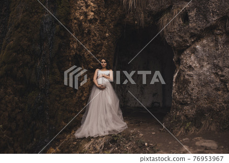 pregnant woman with a big belly in a white long dress near mountains pregnant woman with a big belly in a white long dress near mountains 76953967