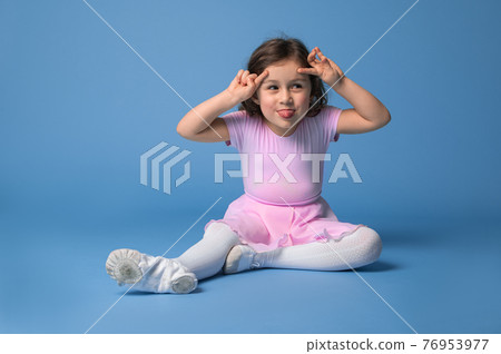 Isolated portrait over blue background of an adorable preschool girl ballerina grimacing and showing her tongue . 76953977