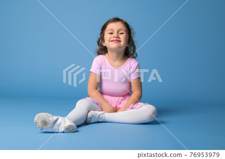 Beautiful and funny little girl in pink dress posing to camera while relaxing on blue background with space for text 76953979