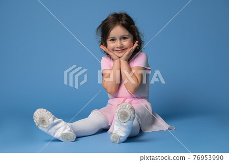 Portrait of an adorable child girl ballerina cute smiling while sitting on blue background Portrait of an adorable child girl ballerina cute smiling while sitting on blue background 76953990