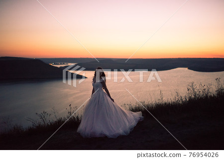 Silhouette of bride in a wedding dress at night against lake and islands Silhouette of bride in a wedding dress at night against lake and islands 76954026
