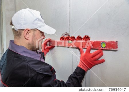 A man, an electrician marks out holes for sockets with a pencil, a tape measure 76954047