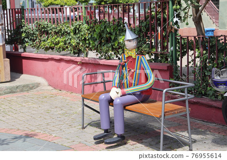 A wooden tourist in a striped shirt sits on a bench, Alanya, April 2021 76955614