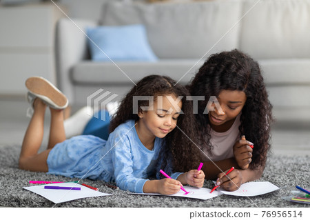 Affectionate black mom drawing with her little daughter on floor at home 76956514