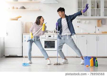 Funny asian couple singing songs while cleaning kitchen, copy space Funny asian couple singing songs while cleaning kitchen, copy space 76956568