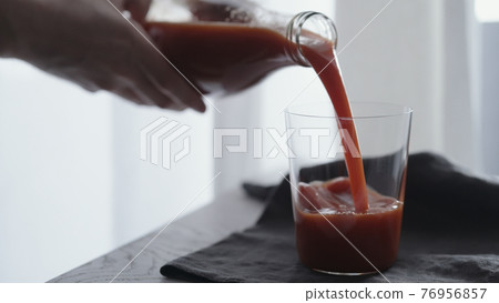man pour tomato juice into tumbler glass on linen cloth 76956857