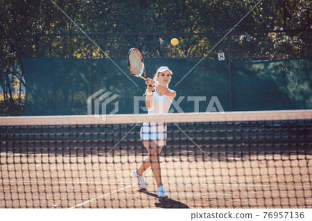 Woman forcefully playing tennis outdoors Woman forcefully playing tennis outdoors 76957136