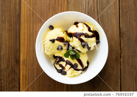Vanilla ice cream scoops sundae in bowl with chocolate syrop on wooden background, copy space Vanilla ice cream scoops sundae in bowl with chocolate syrop on wooden background, copy space 76958197