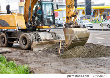 A heavy road excavator flattens a pile of rubble with a bucket when repairing a section of a road. 76958632