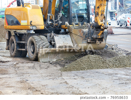 A heavy road excavator smooths a pile of rubble with a bucket at a construction site. A heavy road excavator smooths a pile of rubble with a bucket at a construction site. 76958633