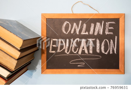 Blackboard with chalk inscription - online learning and a stack of books. Concept of education remotely. Blackboard with chalk inscription - online learning and a stack of books. Concept of education remotely. 76959631