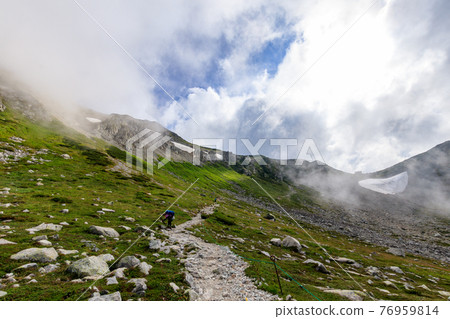 Fantastic cloud-covered snowy valley and climbers Fantastic cloud-covered snowy valley and climbers 76959814