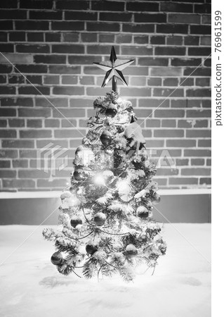 monochrome Christmas tree with festive lights in snow outdoors, brick wall background 76961599