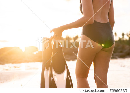 Woman holding flippers in the sea during sunset,Summer holiday and travel concept 76966285