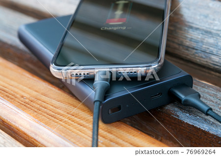 Modern smartphone charges from the power bank on the wooden background. Modern technology. Selective focus. Modern smartphone charges from the power bank on the wooden background. Modern technology. Selective focus. 76969264