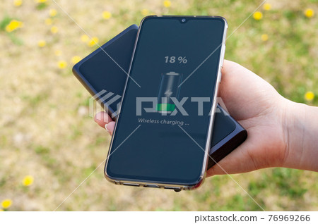 Smartphone charging without cable from induction power bank in the woman hand. Modern technology concept. 76969266