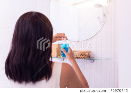 Woman using mouthwash to rinsing mouth in restroom,Fresh breath,Dental health care concept 76970745
