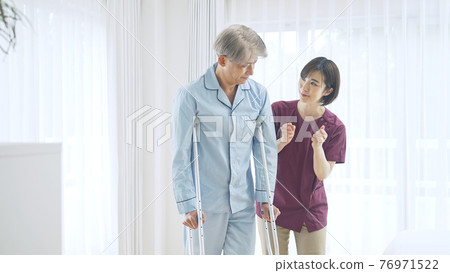 Helper woman assisting with middle-aged man walking on crutches 76971522