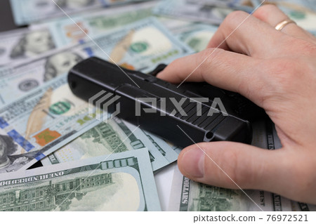 hand holding a gun lies on a pile of money 76972521
