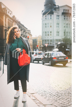 A woman on the street uses a mobile phone. online shopping. use of mobile applications. urban landscape on a background. Film Graine. Noise 76972883