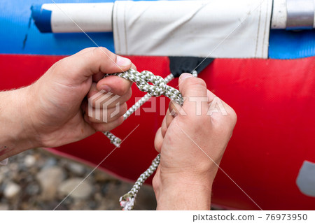 a man holds a knot in hands and ties a rope aboard a boat, ship or yacht a man holds a knot in hands and ties a rope aboard a boat, ship or yacht 76973950