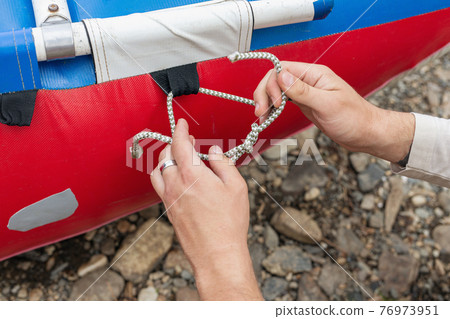 man holds knot in his hands and ties rope aboard boat, ship or yacht man holds knot in his hands and ties rope aboard boat, ship or yacht 76973951