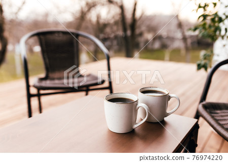 Two cups of coffee on the table on wooden brown terrace during evening sunset 76974220