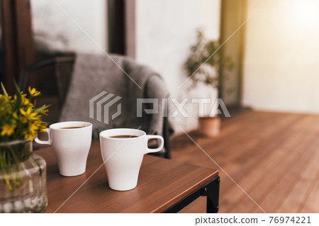 Two cups of coffee on the table on wooden brown terrace during evening sunset 76974221